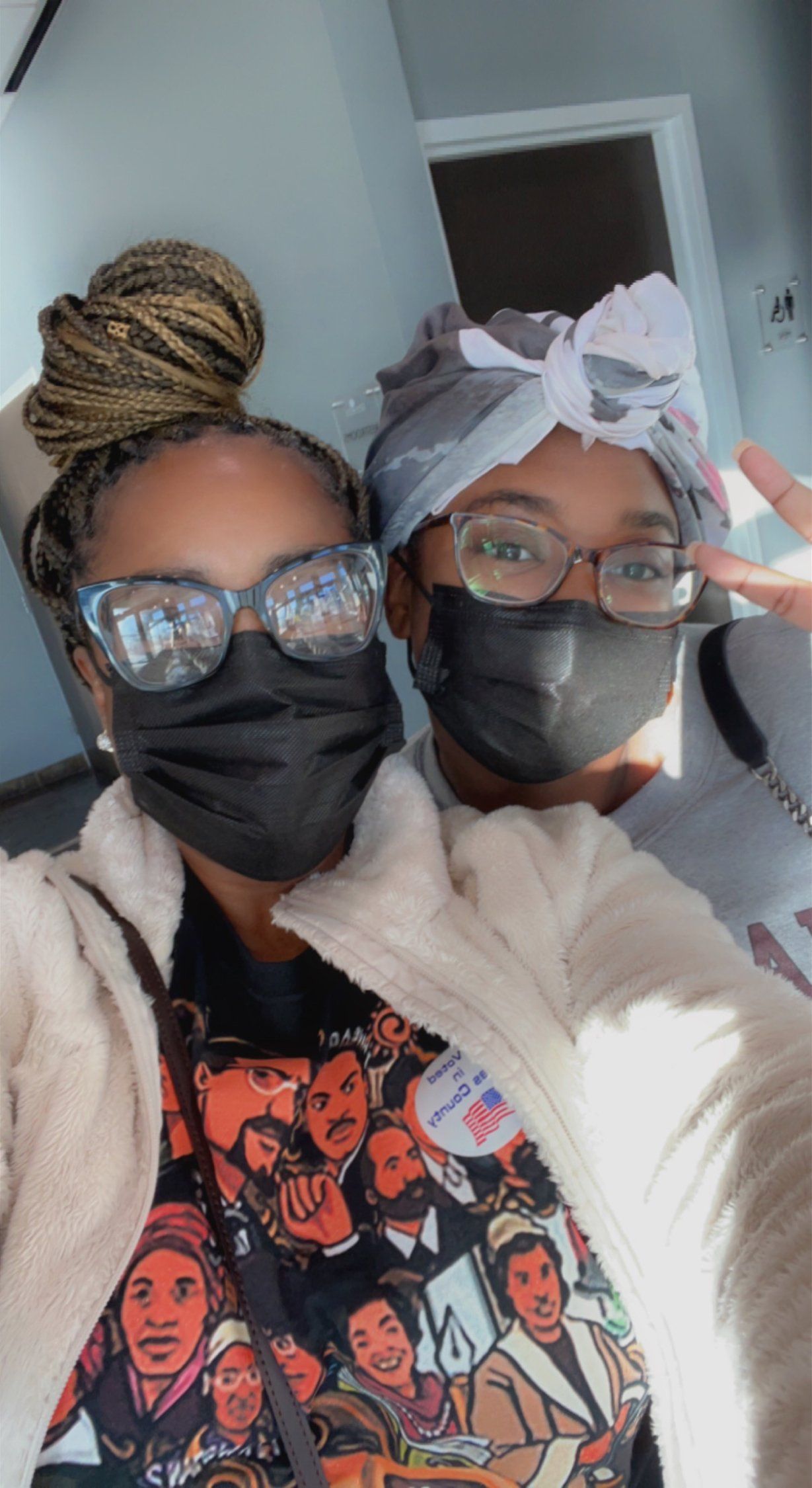 Two people wearing face masks, one with braids, the other with a headscarf, smiling.