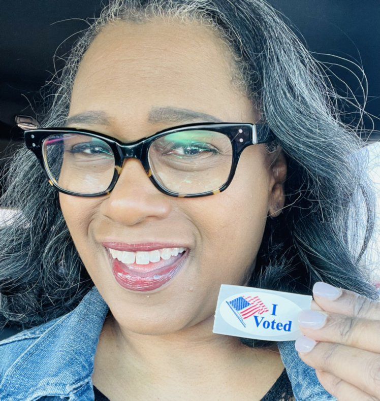 Woman in glasses smiles, holding 