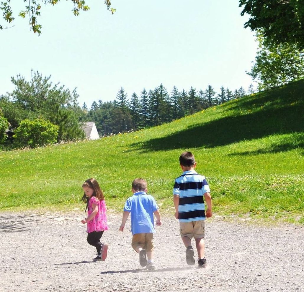 Three children running along a trail in a grassy park