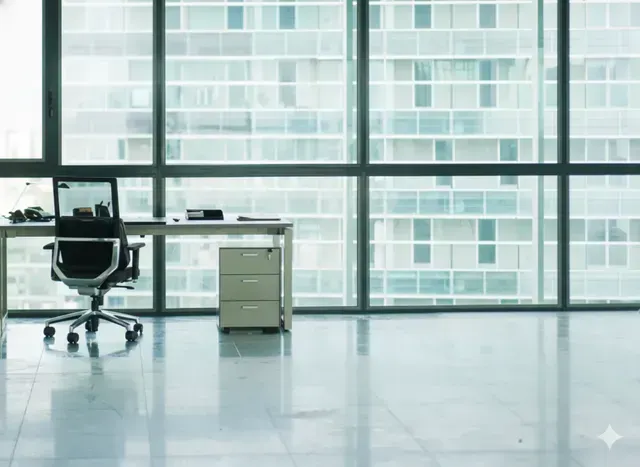 Empty office with desk, chair, and filing cabinet, in front of large windows overlooking a city.