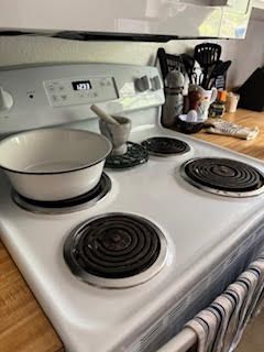White electric stove with a pot, mortar, and kitchen items on the countertop.
