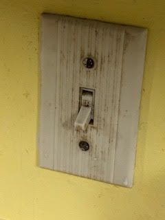 Dirty, white light switch on a yellow wall, switch in the down position.