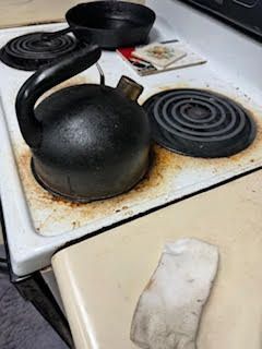 Black kettle on a dirty stovetop next to a skillet and a rag.