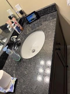 Bathroom vanity with oval sink, dark countertop, and dark brown cabinets.