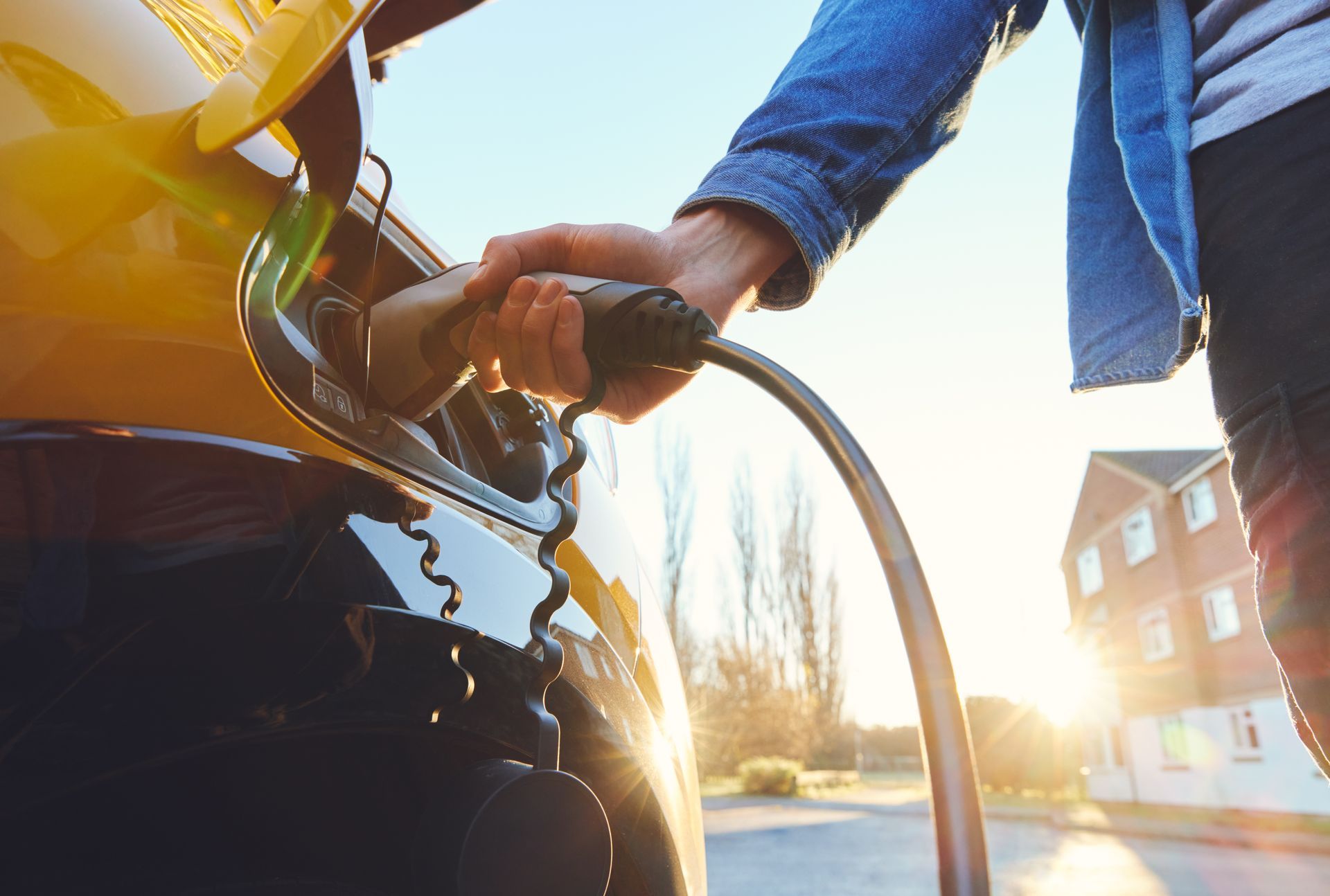 Person refueling a motorcycle at a gas station, with sunlight and a building in the background