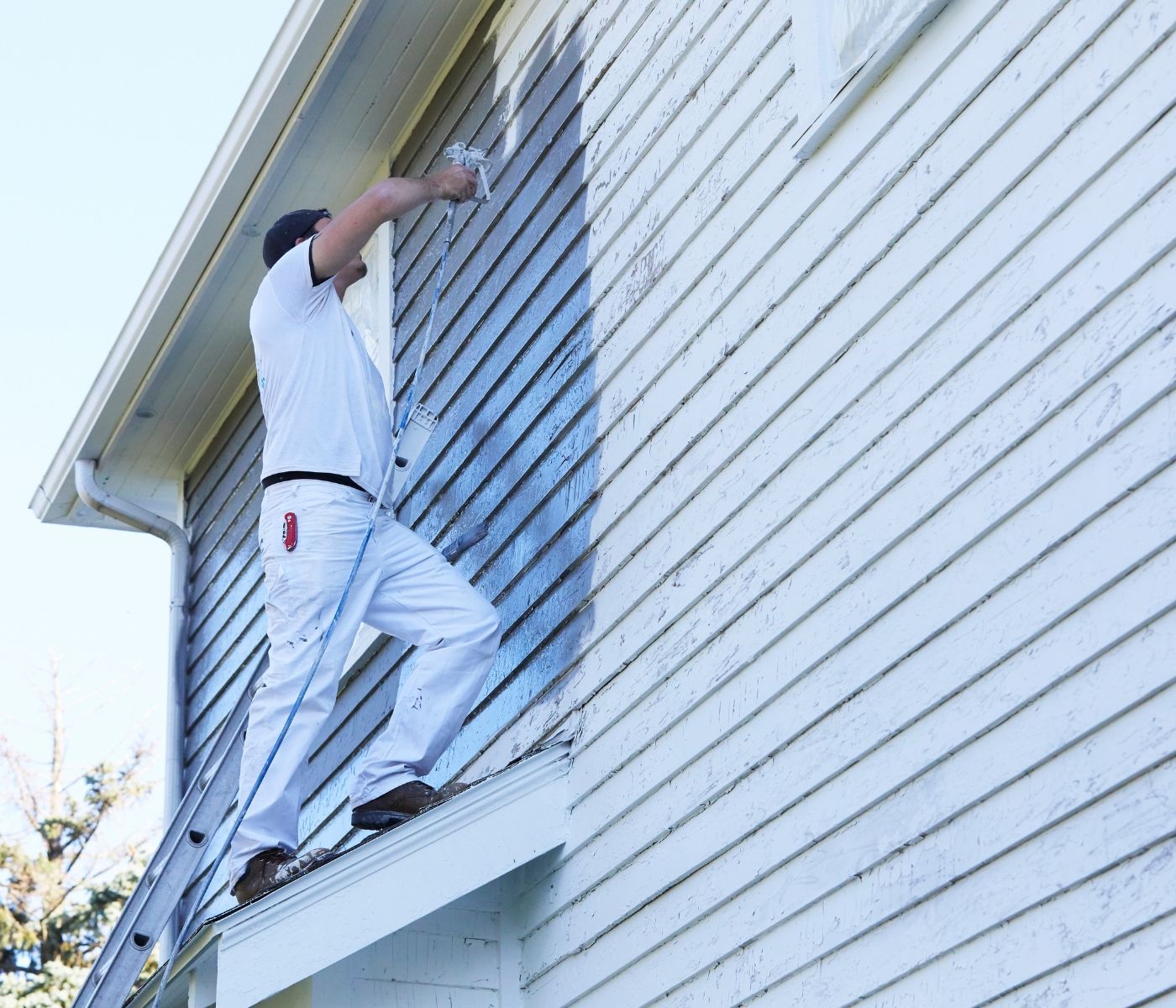 A man is standing on a ladder painting the side of a house.