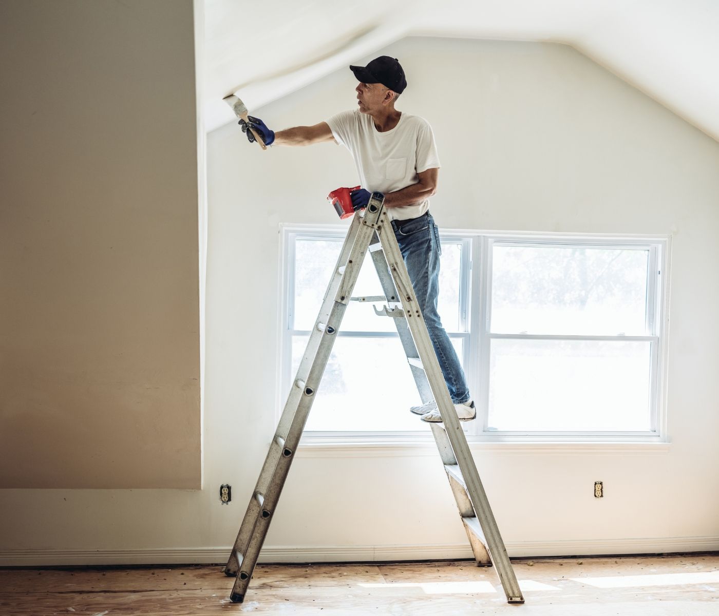 A man is standing on a ladder painting a wall.