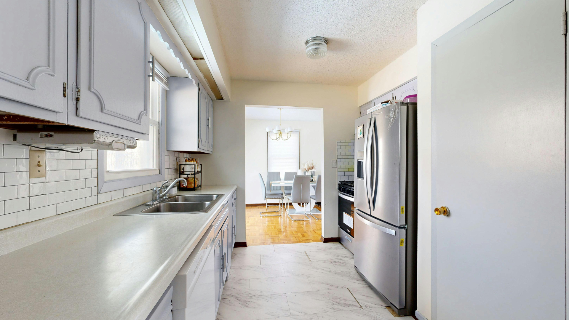 Kitchen with white cabinets, stainless steel refrigerator, and view of dining room.