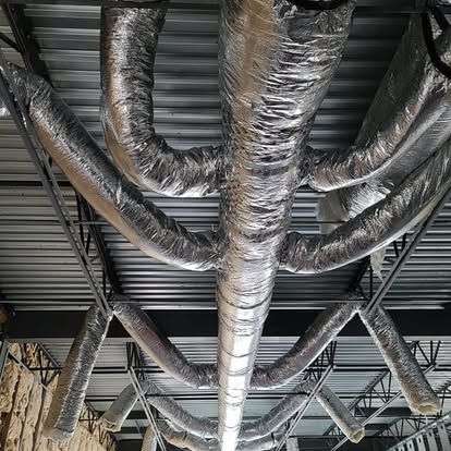 Overhead view of HVAC ductwork, silver insulated flexible tubes branching from a central rectangular duct.
