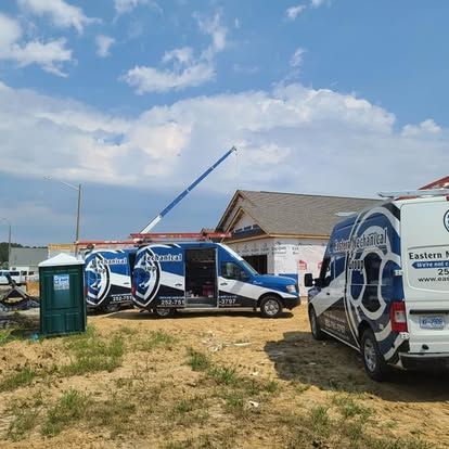 Three Eastern Mechanical service vans parked near a construction site on a sunny day.