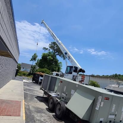 A crane lifting HVAC units from a trailer next to a building on a sunny day.