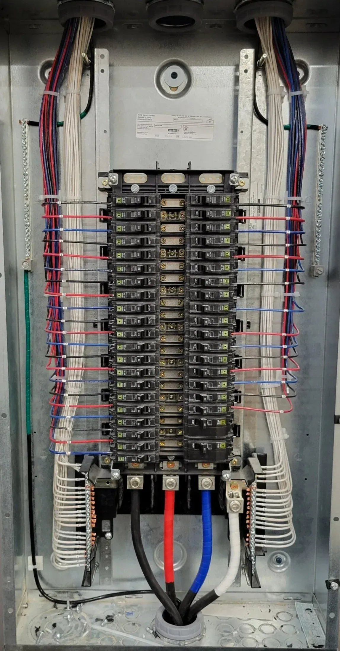 Electrical panel with numerous circuit breakers and color-coded wires.