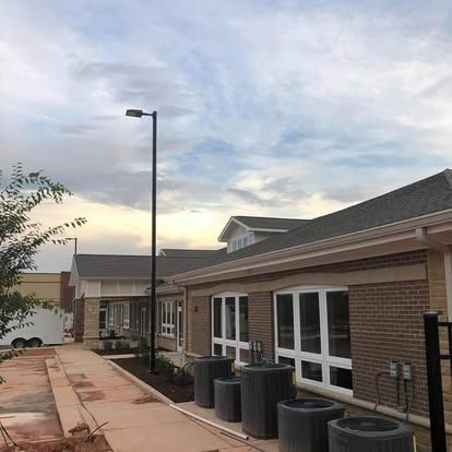 Exterior of a one-story brick building with large windows and a pathway, under a cloudy sky.