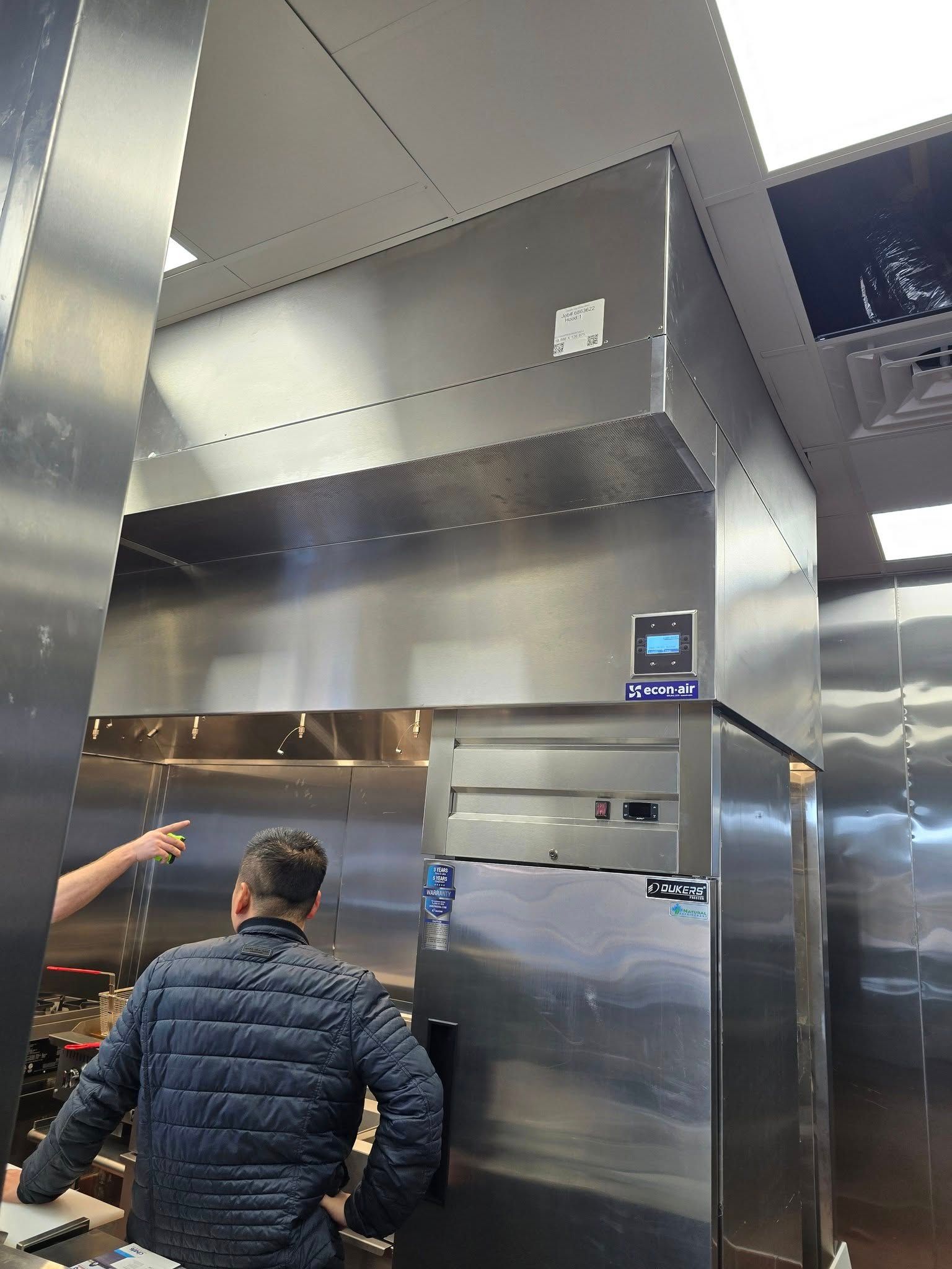 Stainless steel kitchen hood with a control panel, two people near it, one pointing.