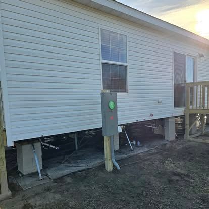 Mobile home with white siding, elevated on concrete blocks. Electrical box in front, deck to the right.