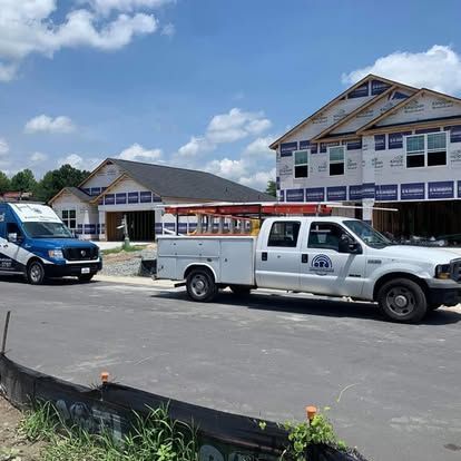White work trucks parked in front of houses under construction on a sunny day.