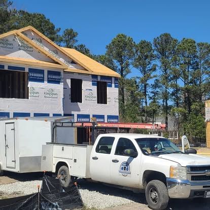 White truck towing a trailer parked at a construction site with a partially built house, sunny day.