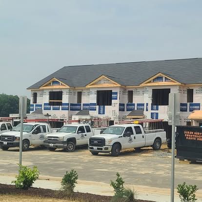 Construction site with multi-unit building under construction, trucks parked in front.