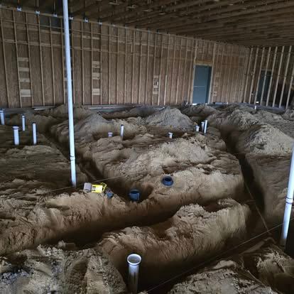 Rough plumbing installation in a dirt floor basement before concrete is poured.