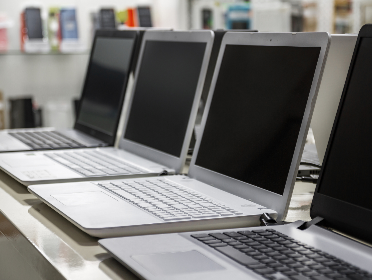 Row of silver laptops on display in a store, screens off.