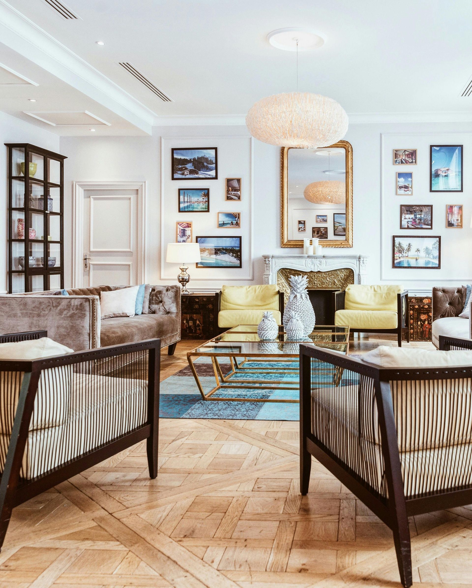 Elegant living room with patterned chairs, gold sofas, blue rug, and framed art on white walls