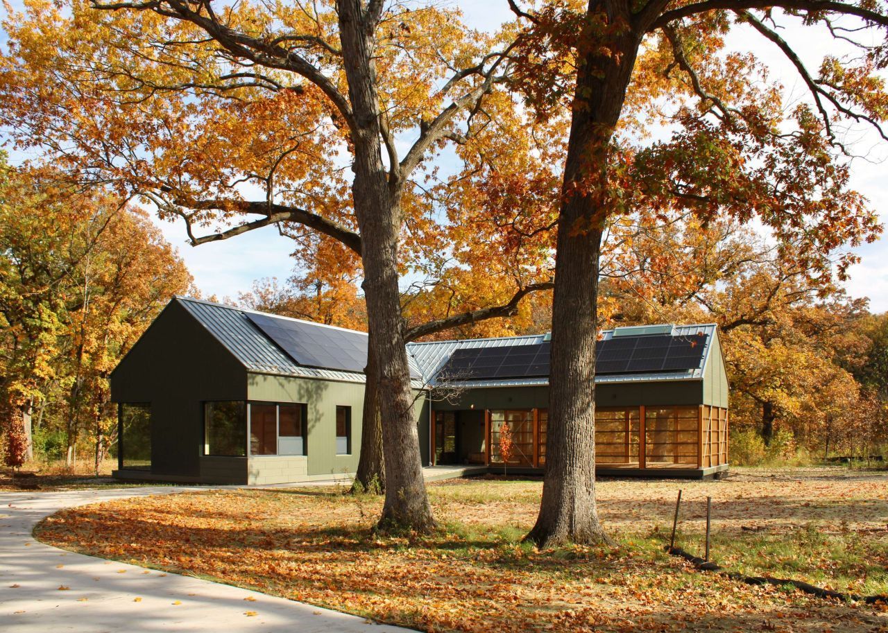 A house with solar panels on the roof is surrounded by trees