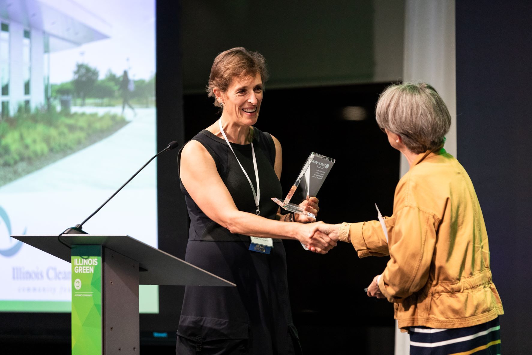 A woman is shaking hands with another woman while holding a trophy.