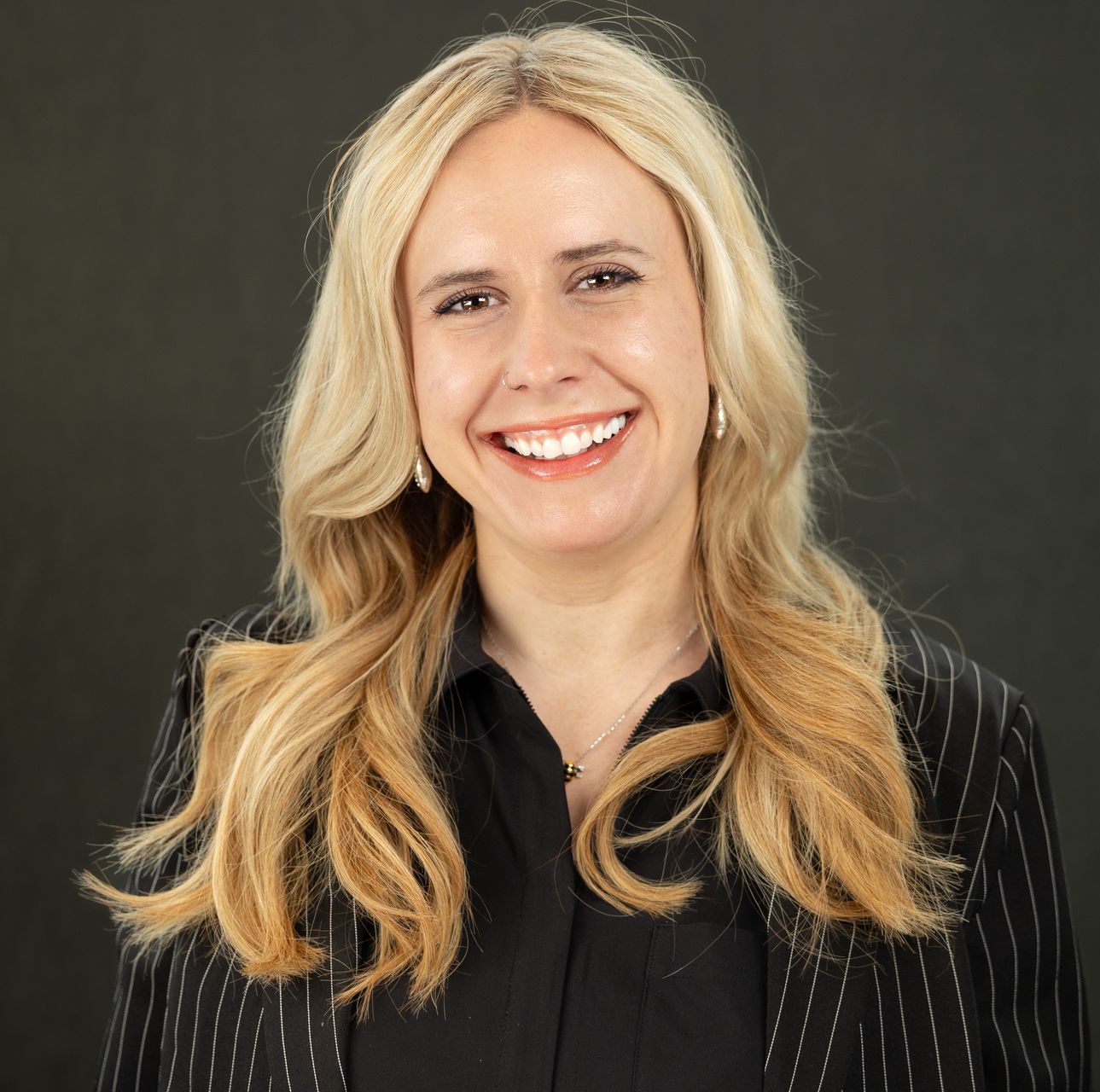 A woman in a striped jacket is smiling in front of a body of water.