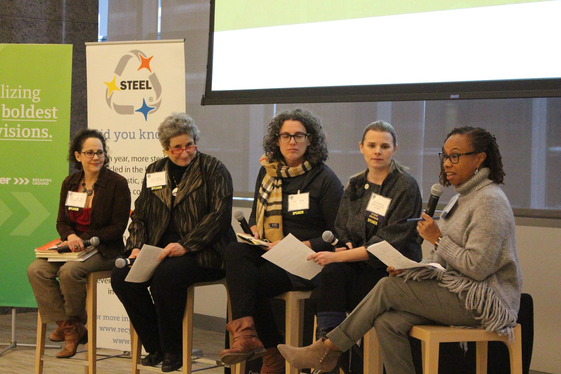 A group of women are sitting on stools in front of a screen.