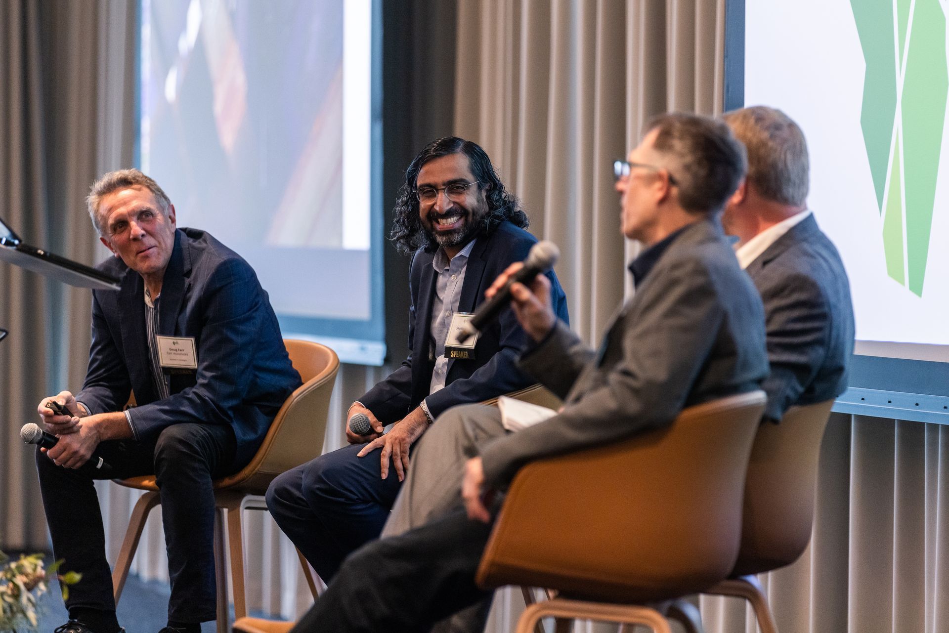 A group of men are sitting in chairs on a stage talking into microphones.