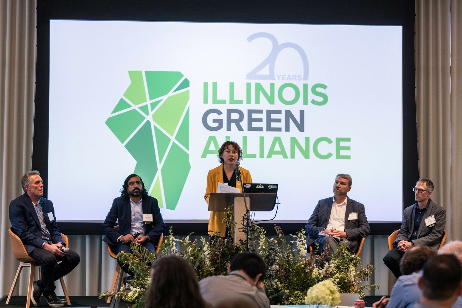 A group of people are sitting in front of a screen that says illinois green alliance.