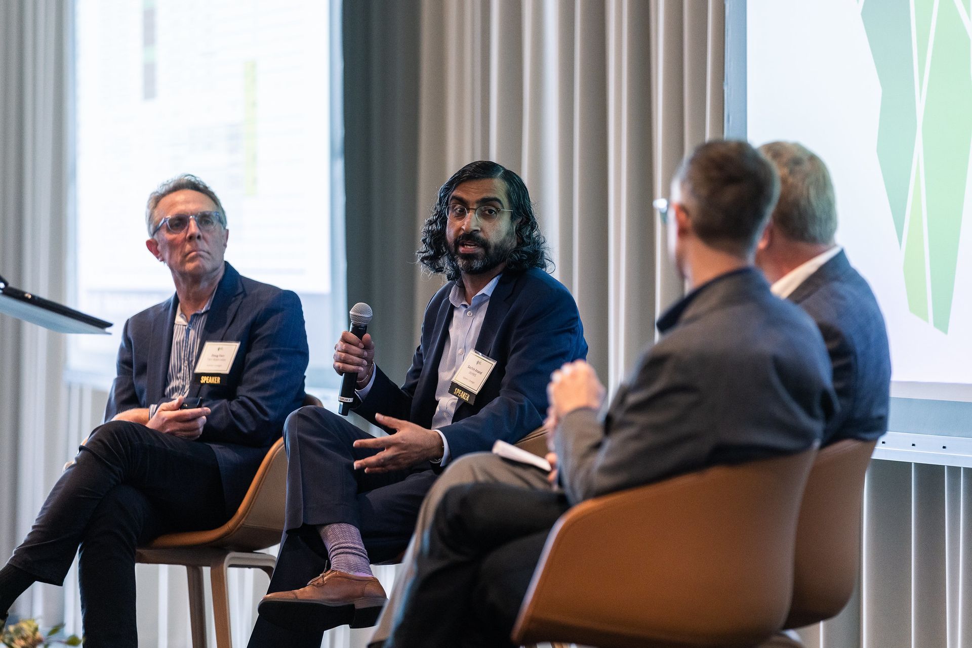 A group of men are sitting in chairs talking to each other at a conference.