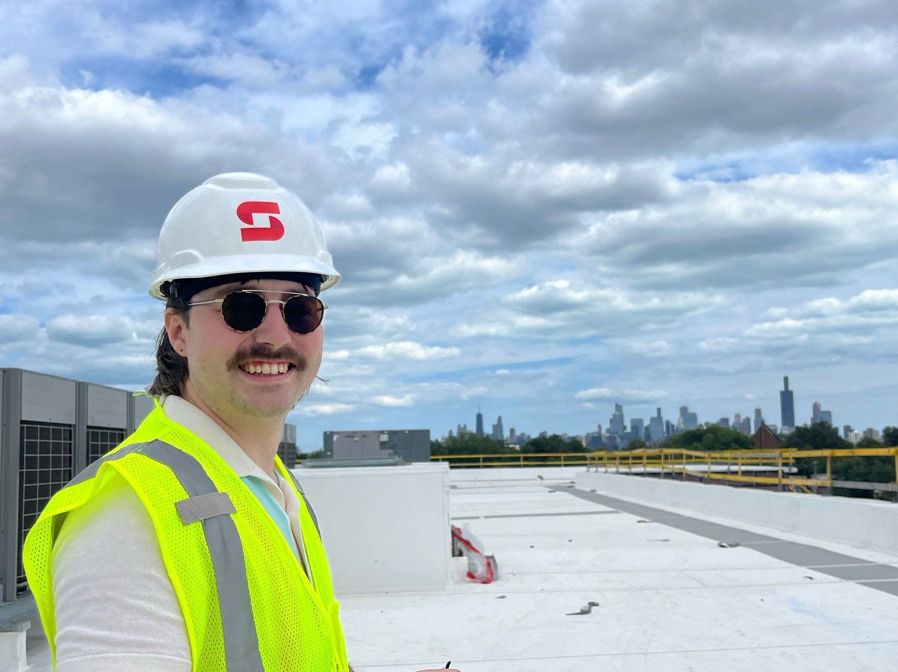 A man wearing a hard hat and sunglasses is standing on a roof.