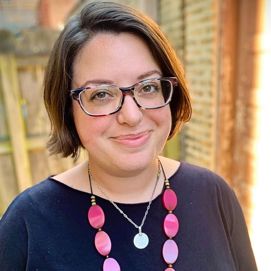 A woman wearing glasses and a pink necklace is smiling for the camera.