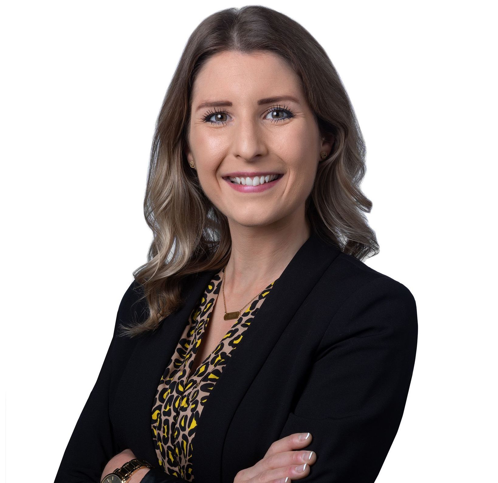 A woman in a black jacket and leopard print shirt is smiling with her arms crossed.