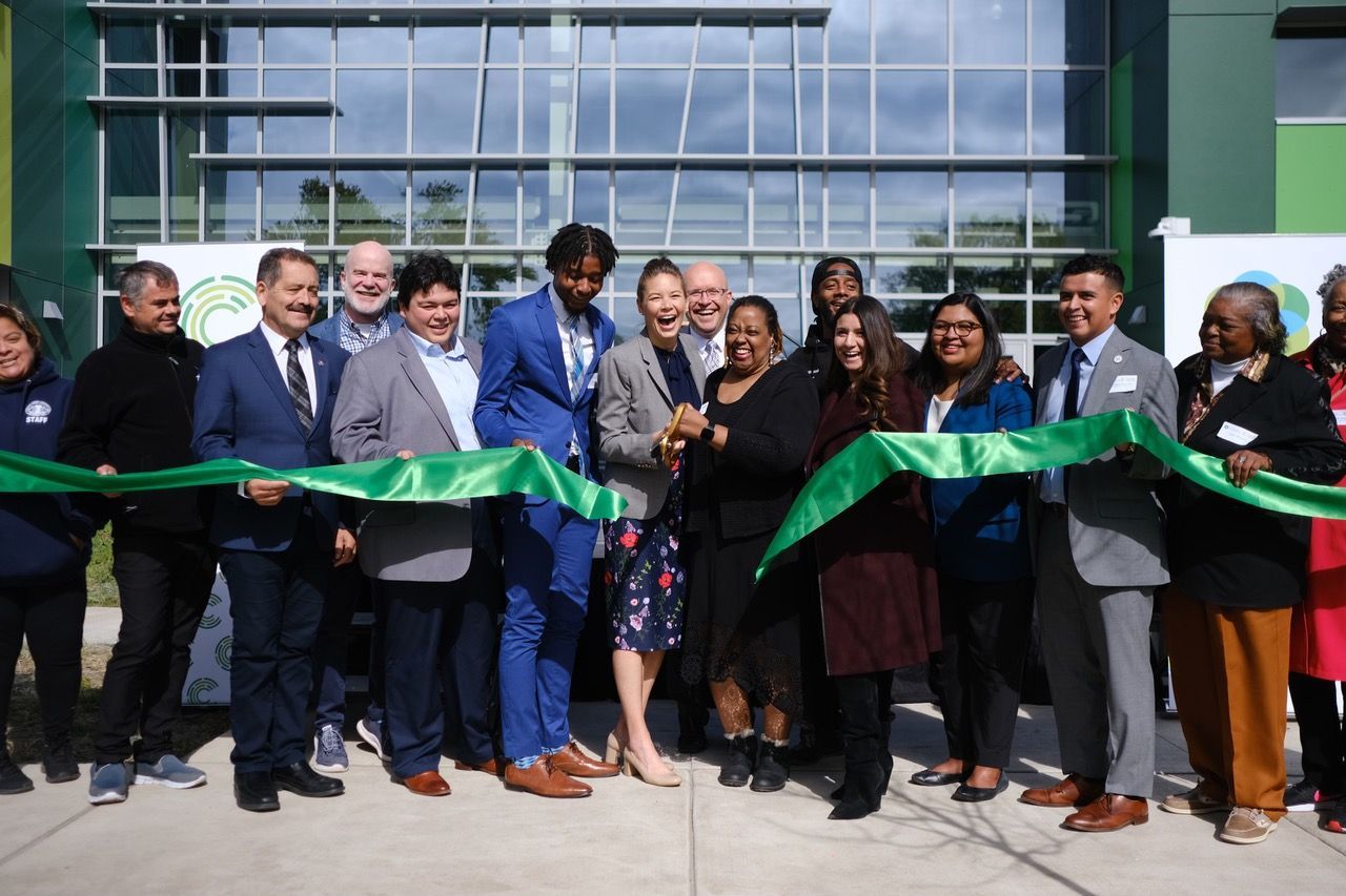 A group of people are cutting a green ribbon in front of a building.