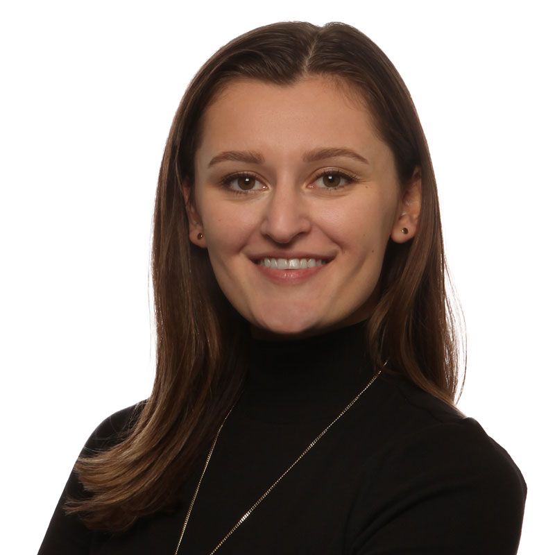 A woman wearing a black turtleneck and a necklace smiles for the camera