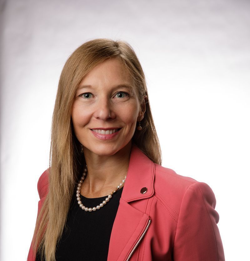 A woman wearing a pearl necklace and a suit jacket smiles for the camera