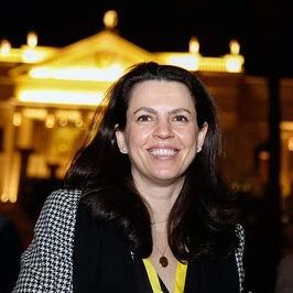 A woman is smiling in front of a building at night.