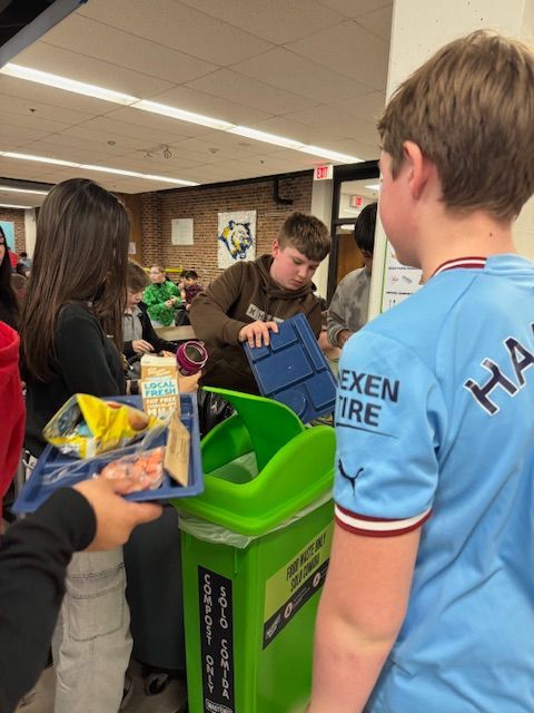 A man is kneeling down next to a blue trash can.