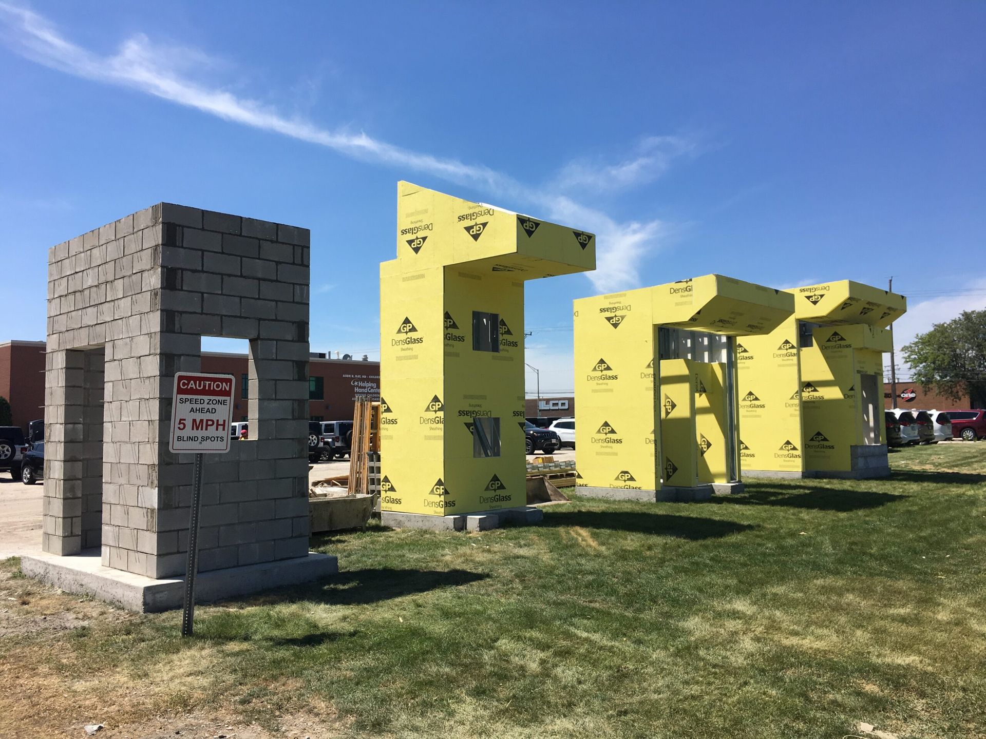 A large sculpture made of bricks and yellow styrofoam is sitting in a grassy field.