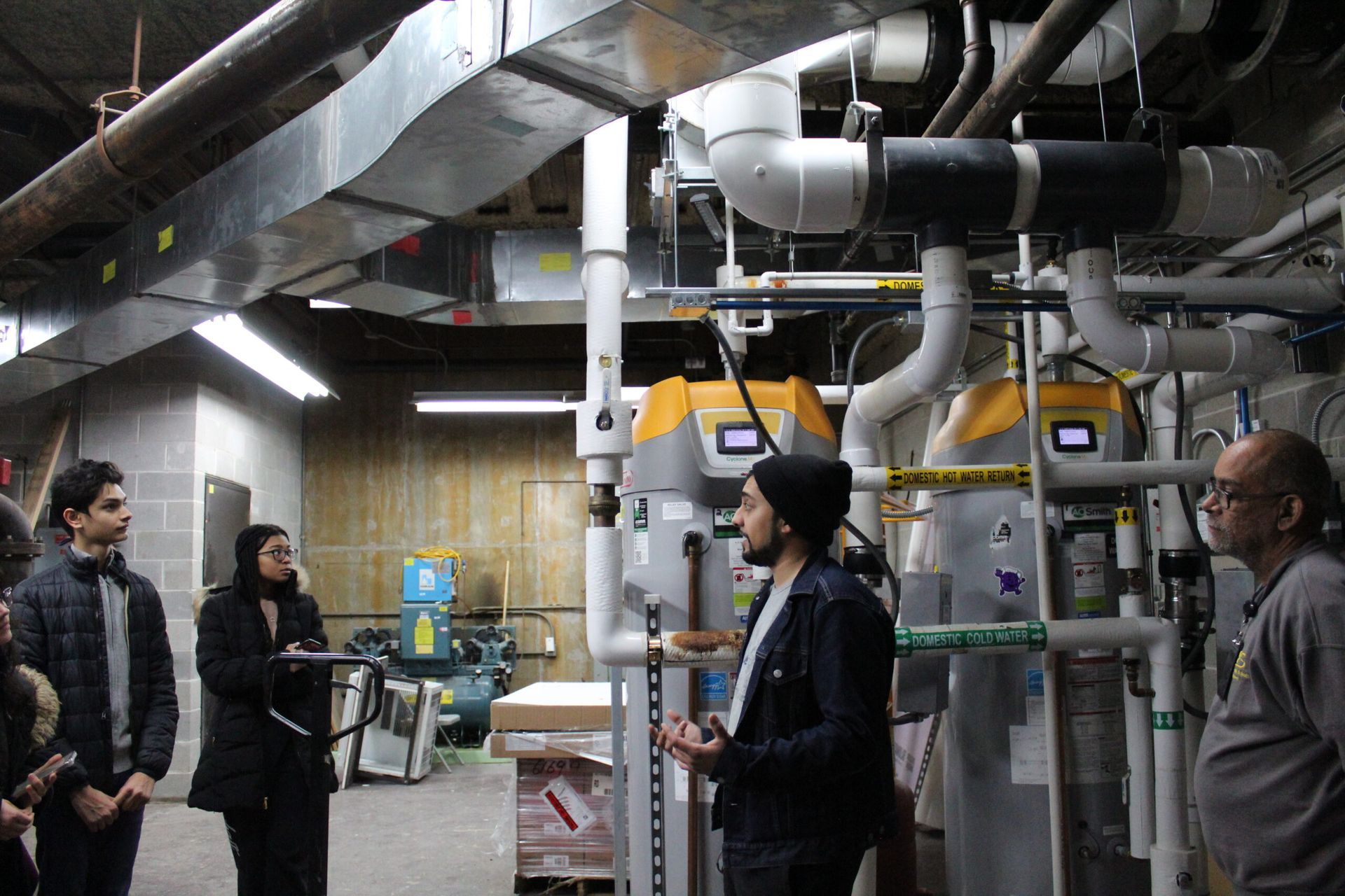 A group of people are standing in a room with pipes.