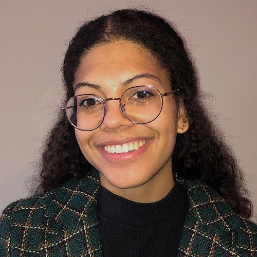 A woman wearing glasses and a green jacket is smiling for the camera.