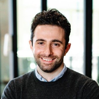 A man with a beard and a gray sweater is smiling for the camera.