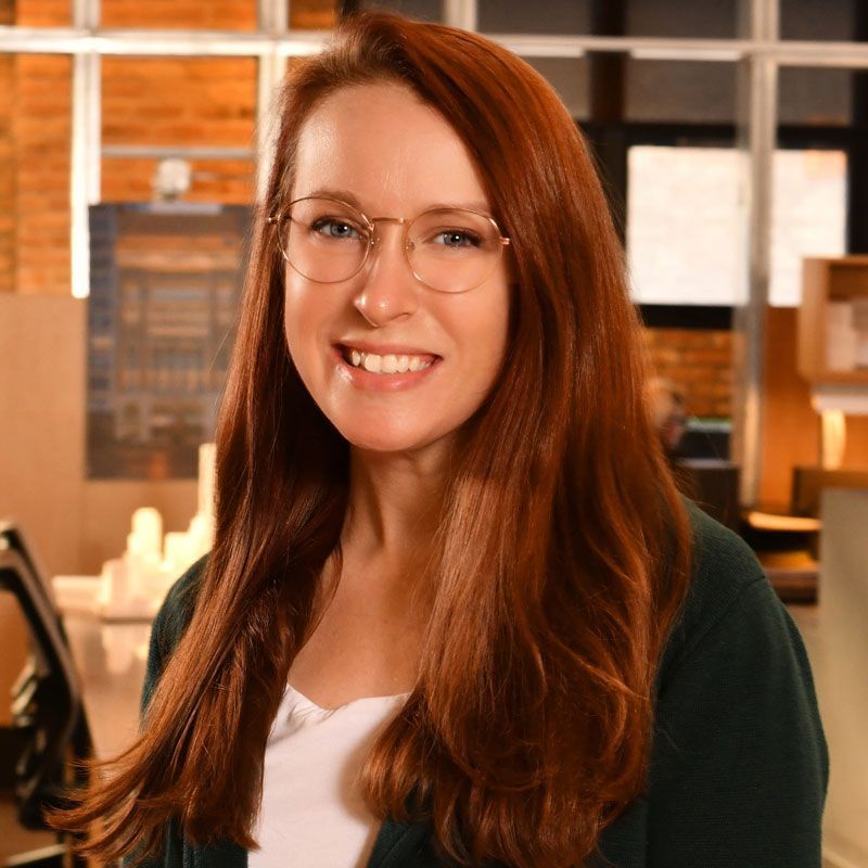 A woman with red hair and glasses is smiling for the camera