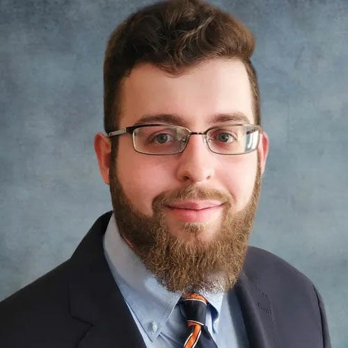 A man with a beard and glasses is wearing a suit and tie.