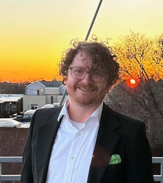 A man in a suit and white shirt is smiling in front of a sunset