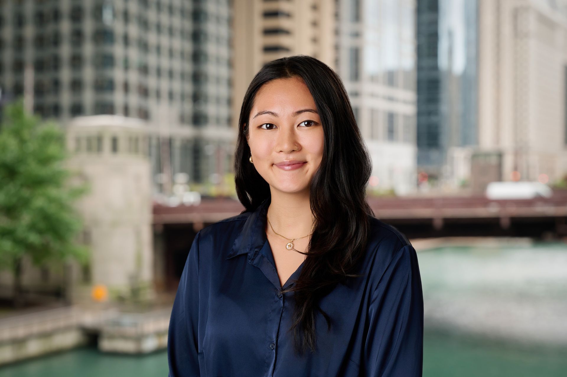 A woman in a black jacket is smiling in front of a city skyline.