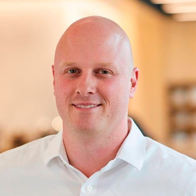 A man with glasses and a beard is wearing a suit and a black shirt.