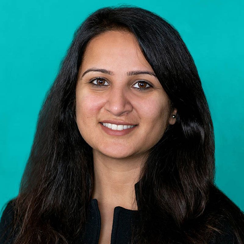 A woman with long dark hair is smiling in front of a blue background.